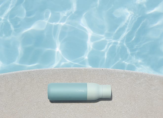 Larq bottle with light blue sleeve on the sun near swimming pool